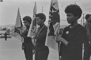 Three African American women wearing black standing holding flags.