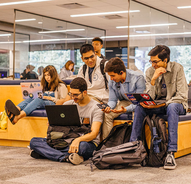 Students gathered around their laptops in a campus library.