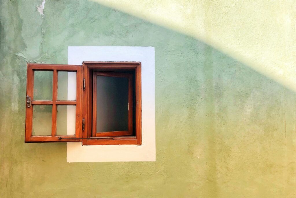 A photo of an open window on a green and yellow painted wall.
